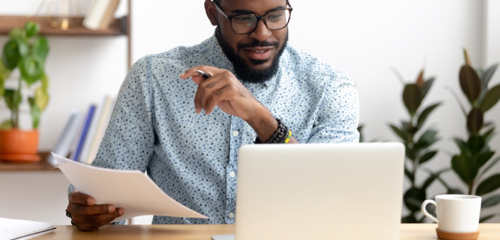Homme regardant un ordinateur avec une fiche de paie dans la main