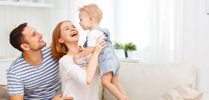 Un père (brun) regardant un bébé (roux) tenu par la mère (roux), tous les trois heureux